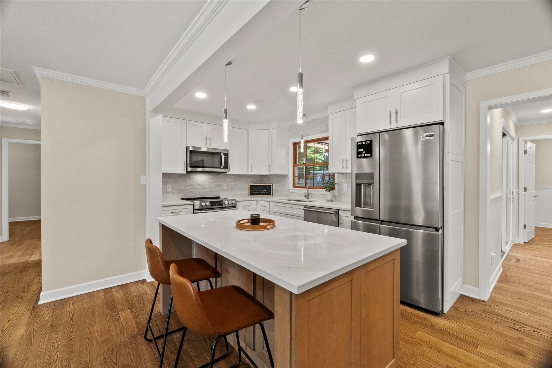Bright modern kitchen with white island, stainless steel appliances, and wood floors