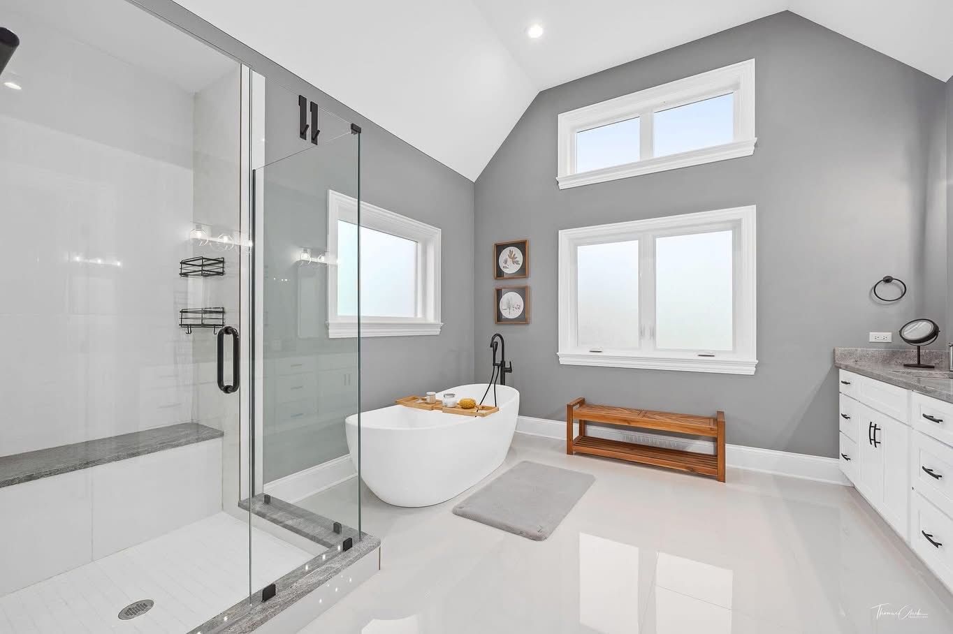 Bright modern bathroom with glass shower, freestanding tub, window, and white vanity