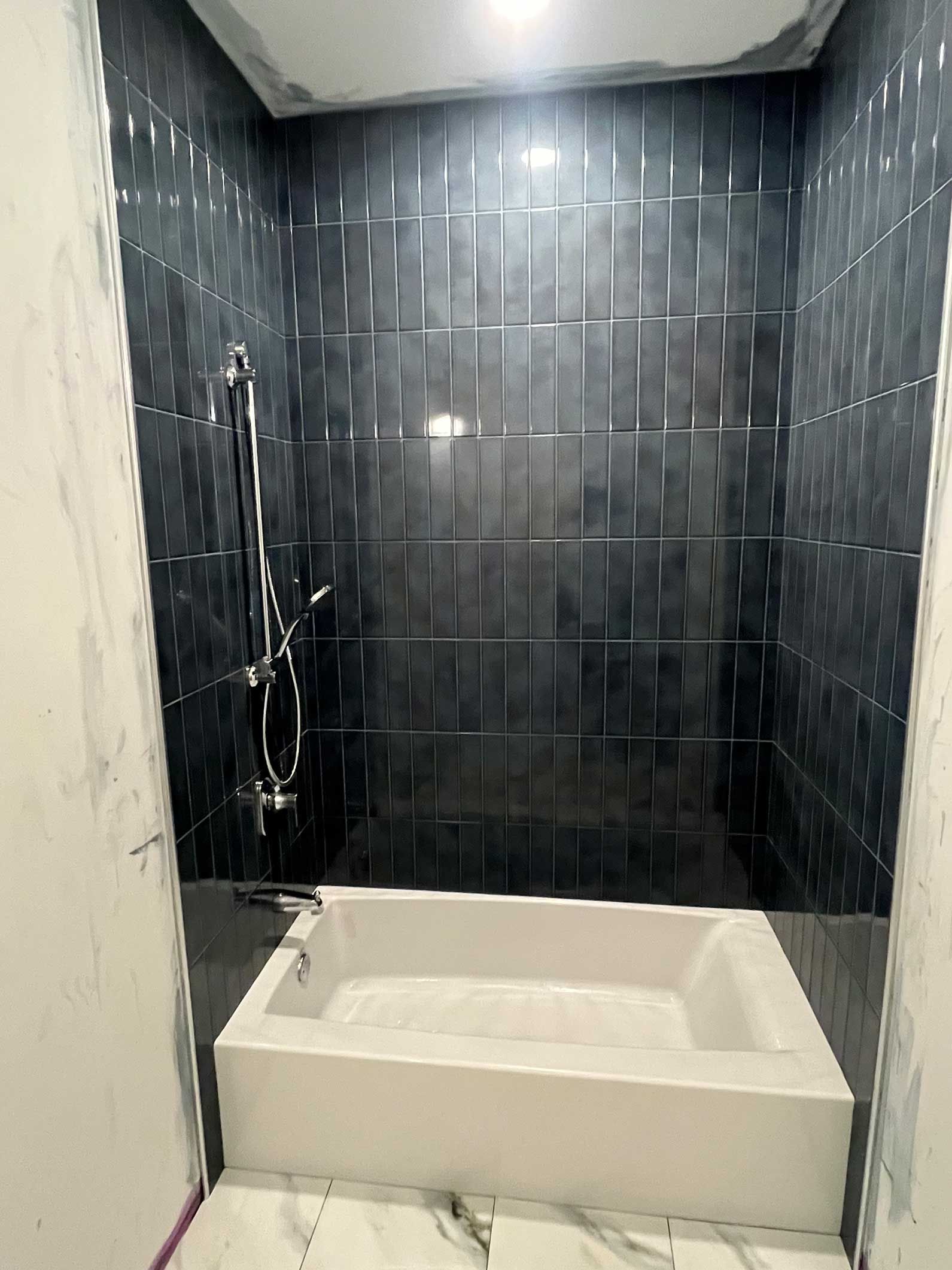 Modern bathroom shower with white tub, dark tiled walls, and handheld showerhead