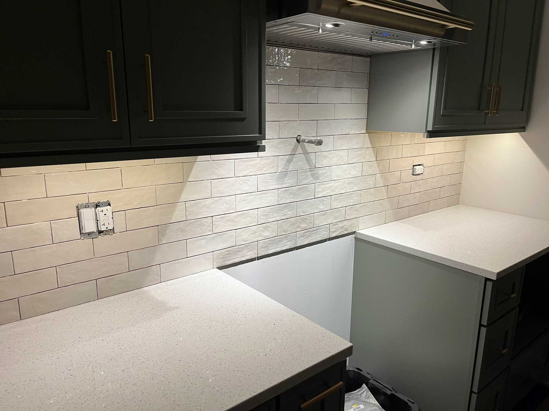 Empty kitchen with white countertops, dark cabinets, and white tile backsplash under a range hood