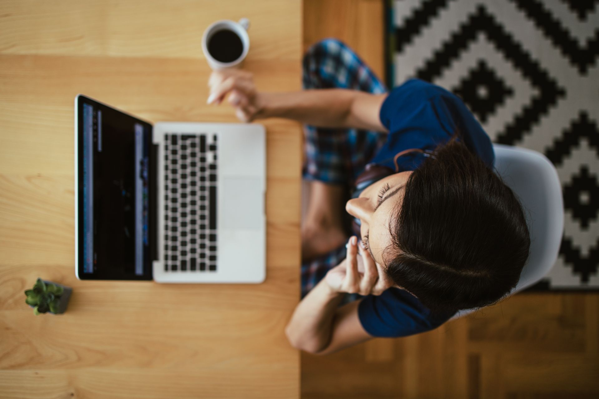 A woman is sitting at a desk with a laptop and a cup of coffee.