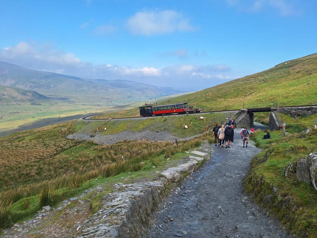 A group of people are walking down a dirt road with a train in the background.