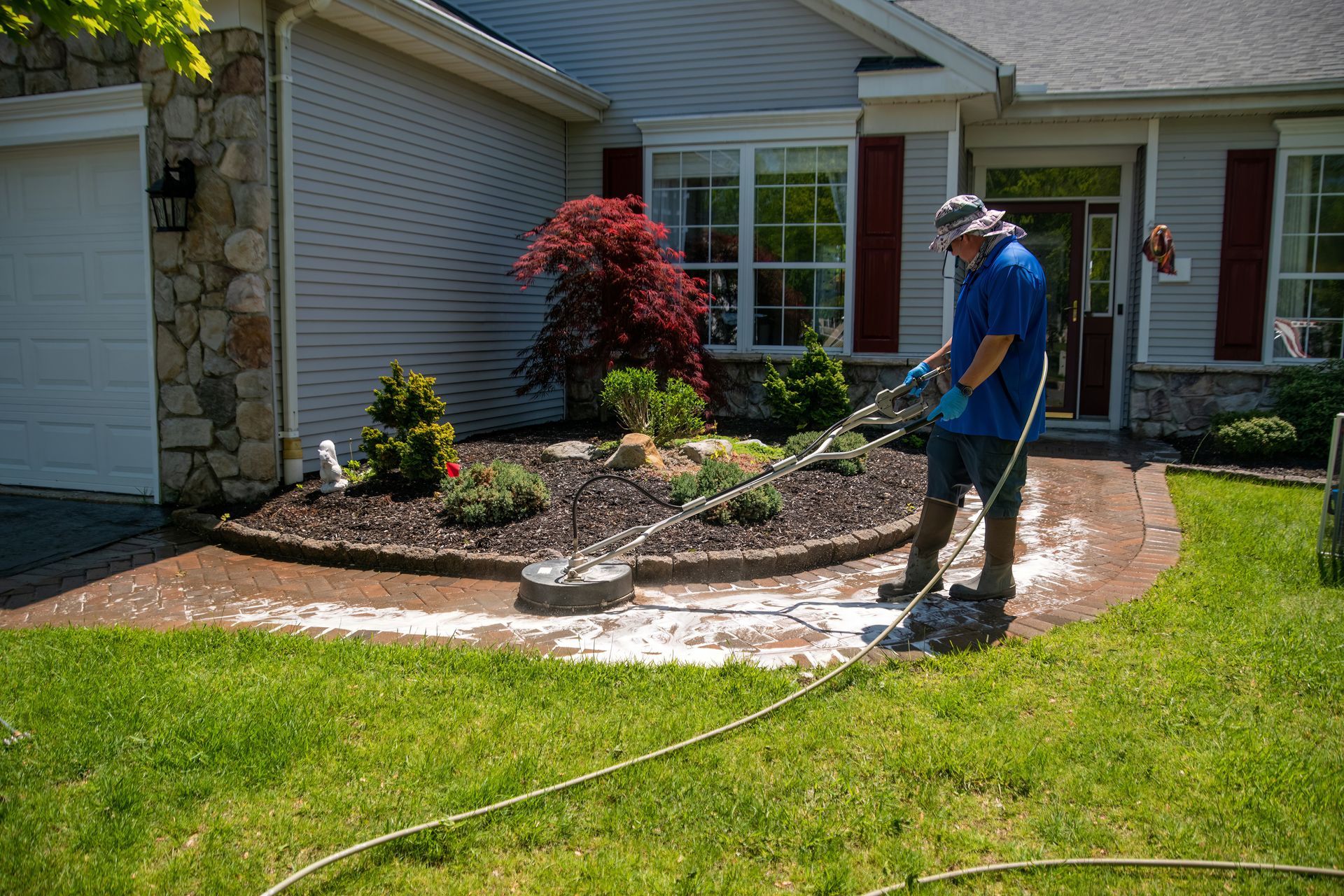 Person pressure washing a curved concrete walkway in front of a house, cleaning debris.