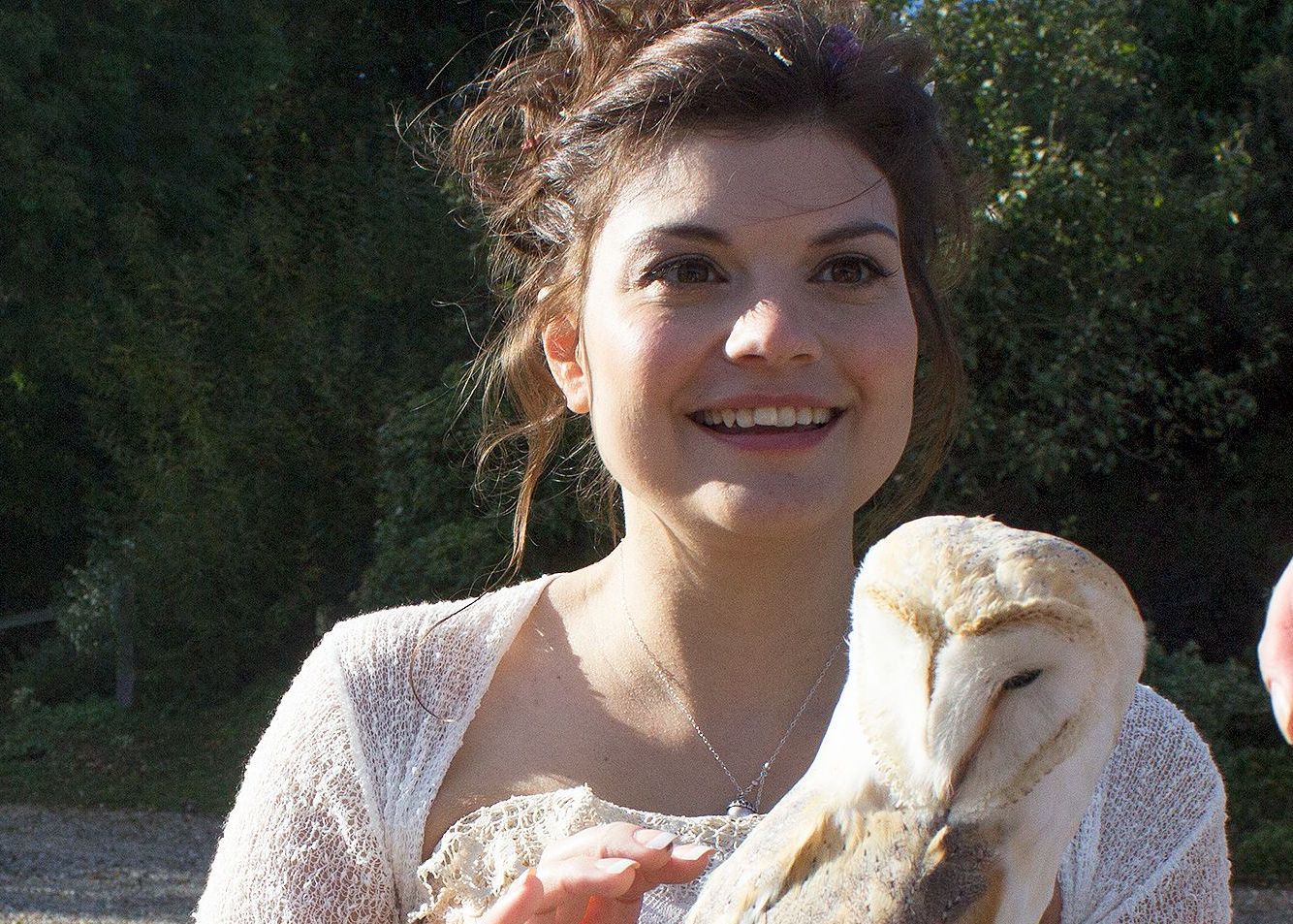 A woman is holding an owl in her hands and smiling.