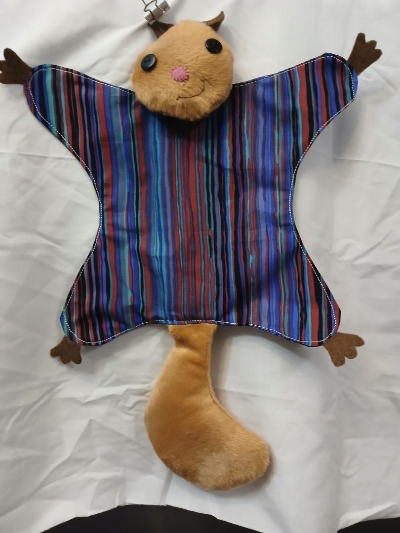 Tan plush cat with striped shirt, outstretched arms, and a long tail on white fabric background