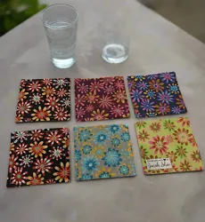 Six colorful patterned coasters on a table beside a glass of water and a small dish.