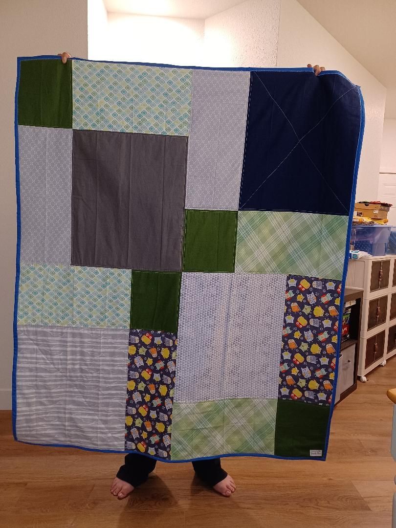 Person holding a large patchwork quilt indoors, with feet visible at the bottom.