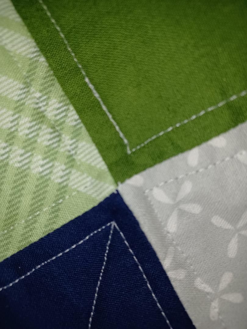 Close-up of green, blue, and white patterned fabric with stitched seams and floral accents