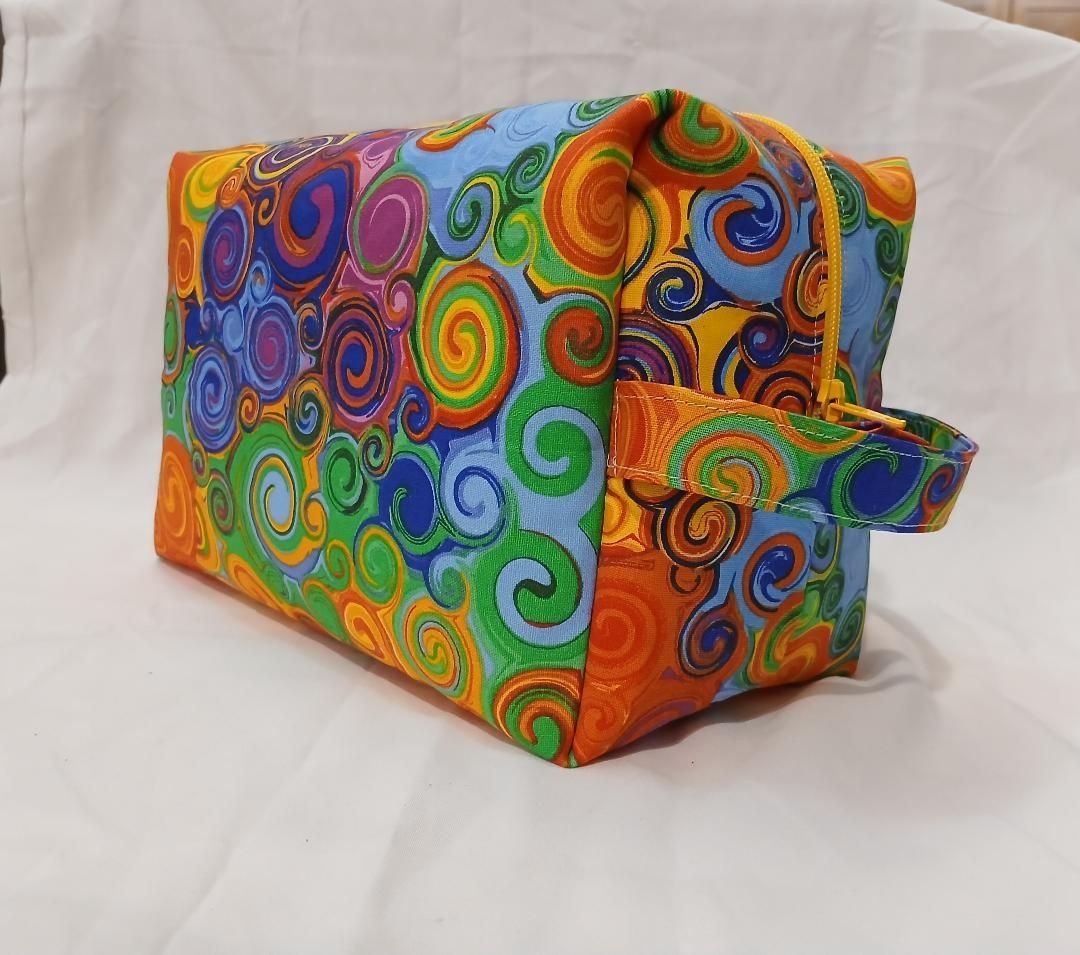 Colorful spiral-patterned fabric toiletry bag with a side pocket on a white background