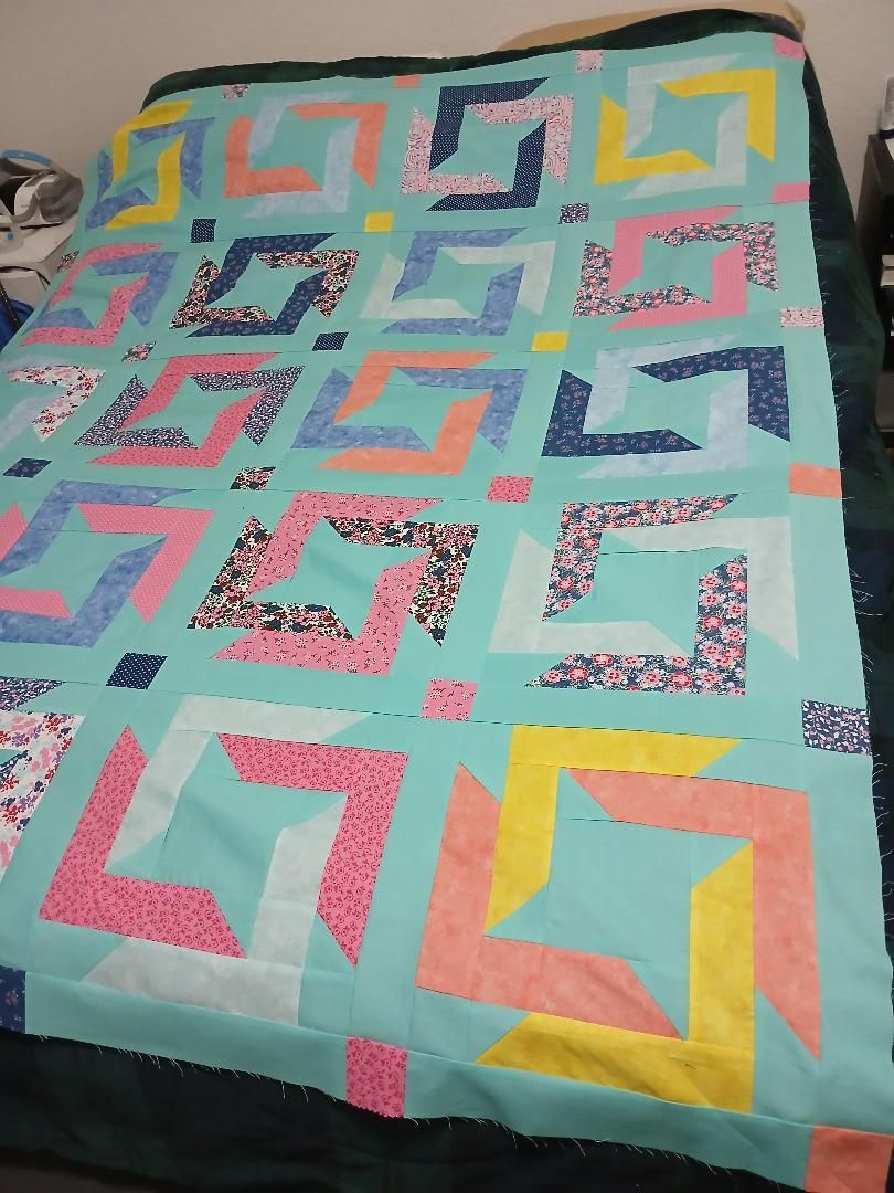 Colorful patchwork quilt with geometric square patterns in teal, pink, yellow, and blue on a bed.