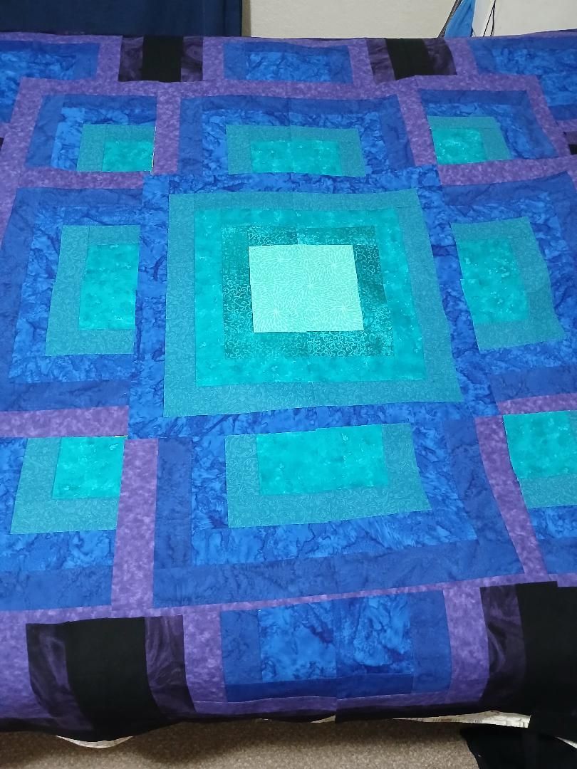 Blue and purple geometric quilt with square patterns and a light turquoise center