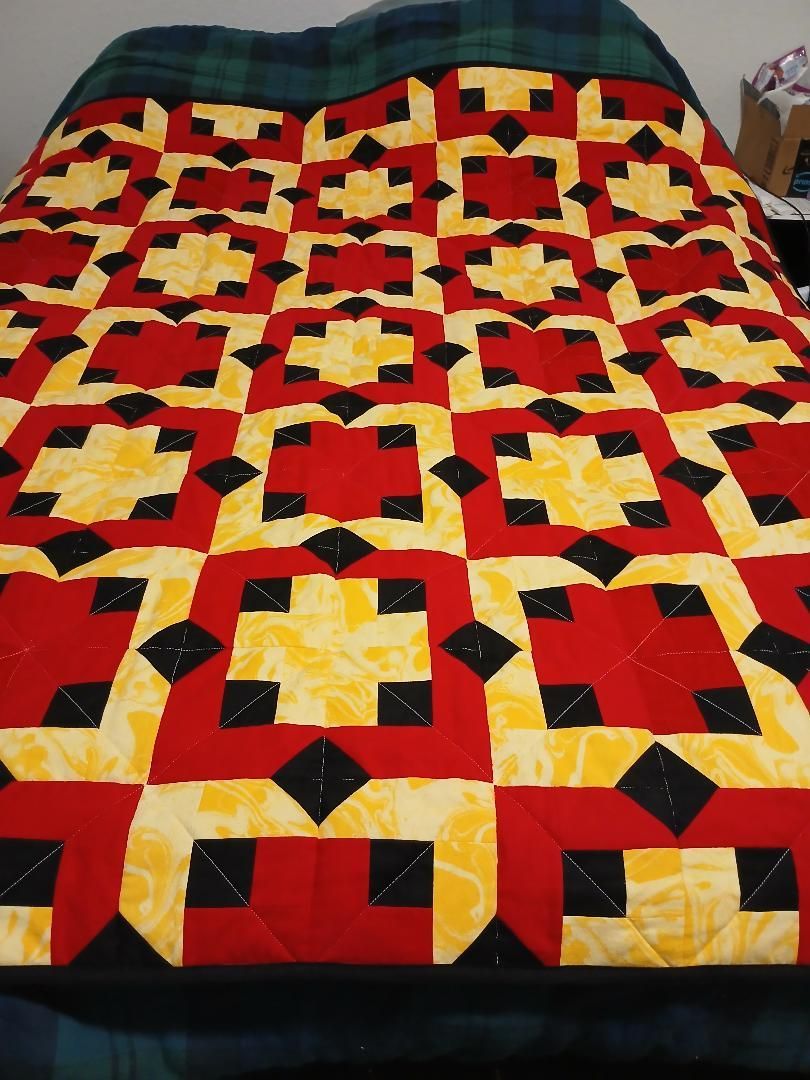 Colorful red, yellow, black, and white patchwork quilt spread over a bed