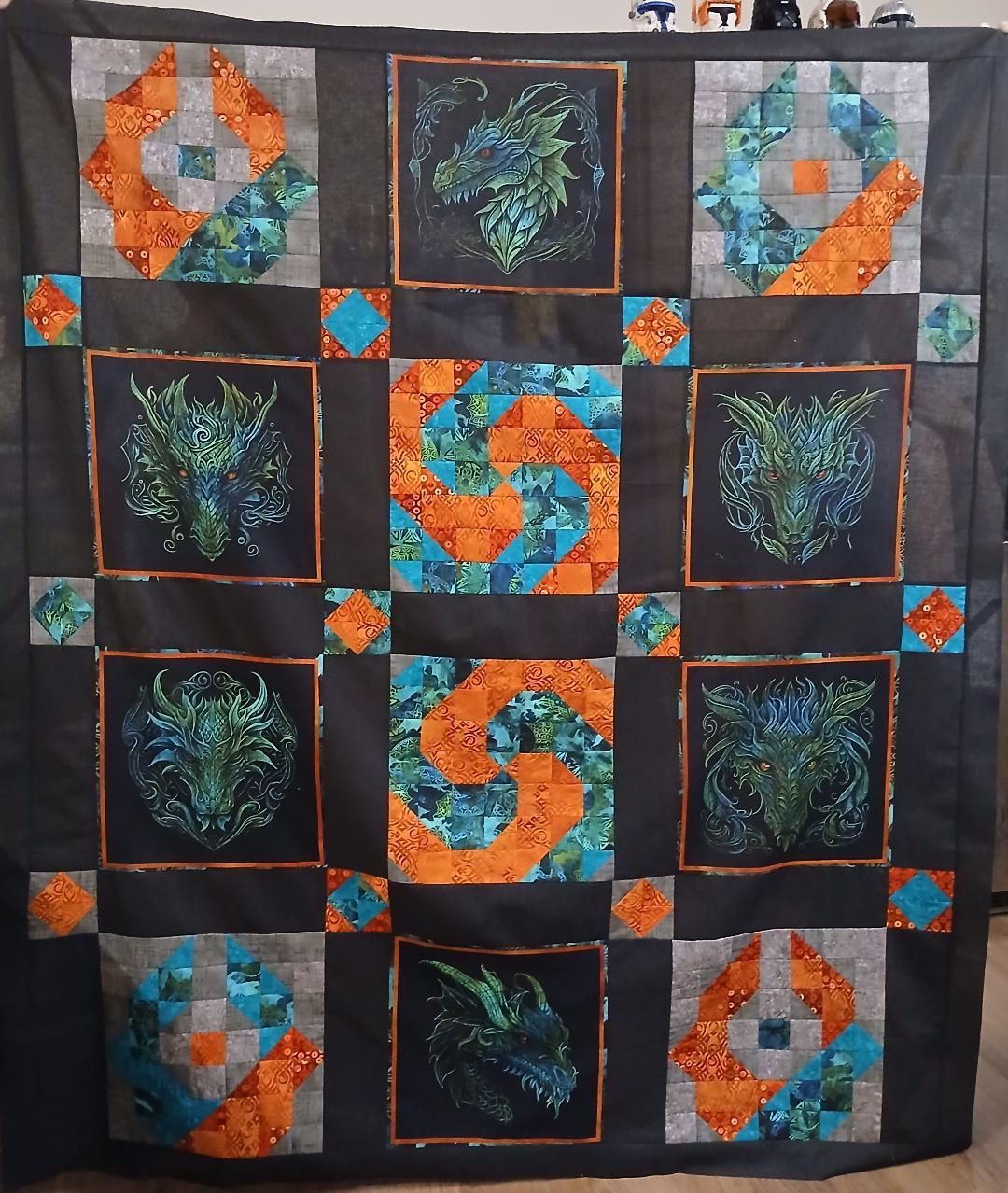 Patchwork quilt with orange, teal, black, and green square blocks in a grid pattern.