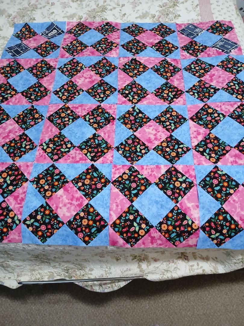 Colorful patchwork quilt with pink, blue, and floral diamond blocks on a textured surface
