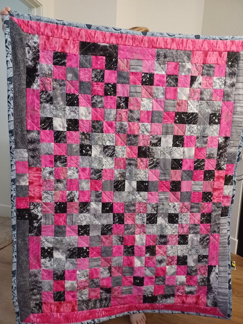 Pink and gray patchwork quilt with a checkerboard pattern hanging on a wall