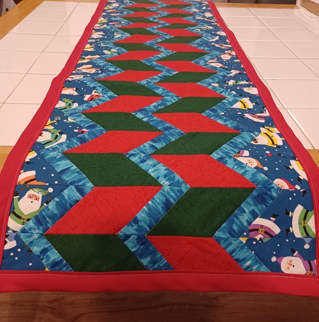 Colorful geometric quilt runner on a tiled floor with red border and blue patterned sides