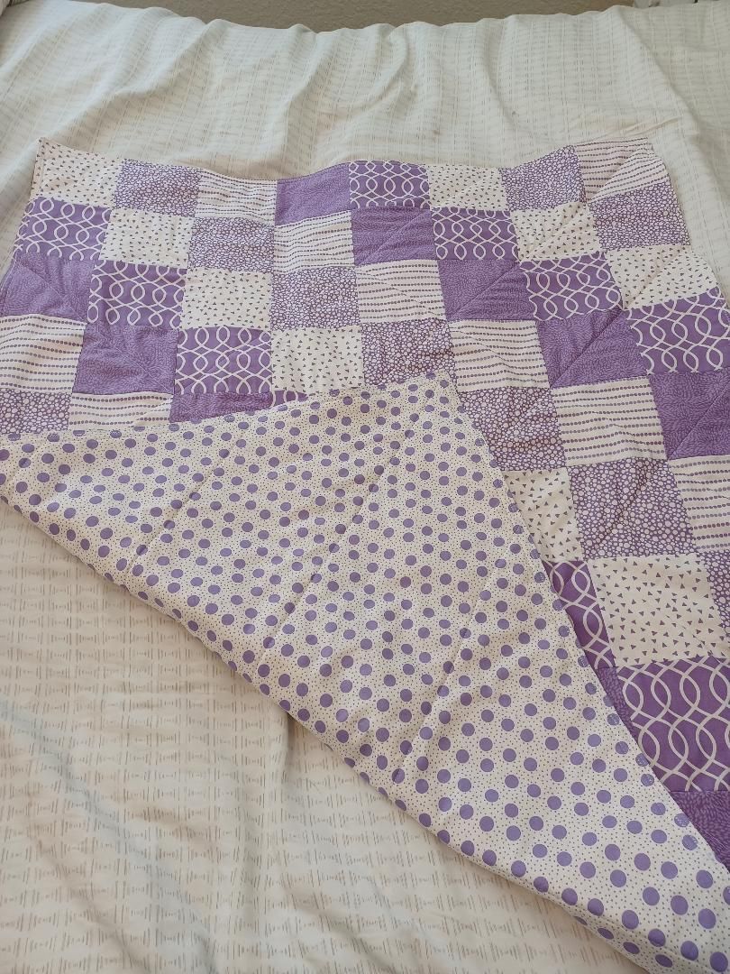 Purple-and-white patchwork quilt with polka dots and floral patterns draped on a bed