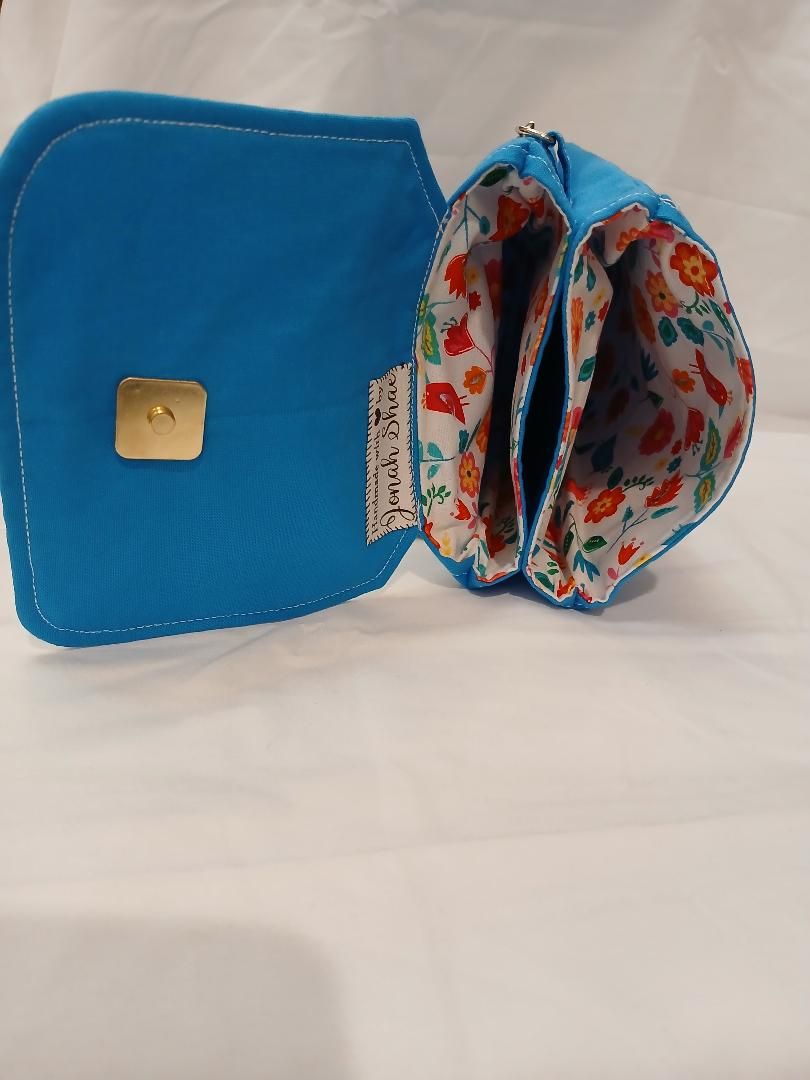 Blue coin purse with floral lining and a small gold clasp, open to show the patterned interior.