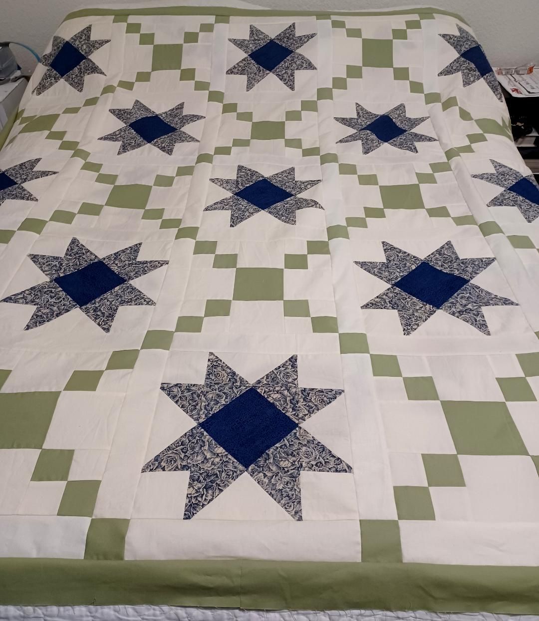 Quilt on a bed with blue star blocks and green checkerboard borders.
