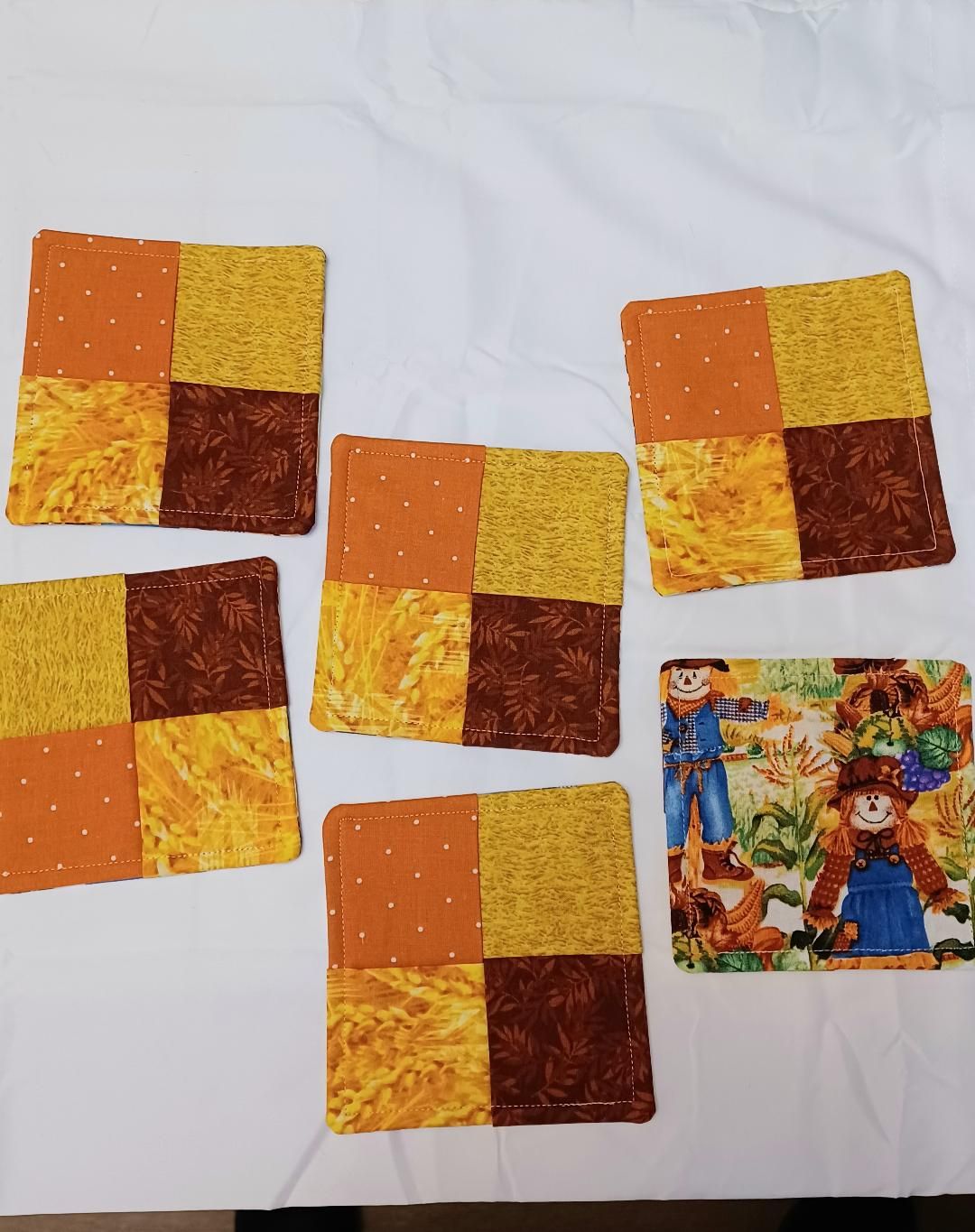 Five orange-yellow quilt squares and one colorful anime-style card on a white cloth background