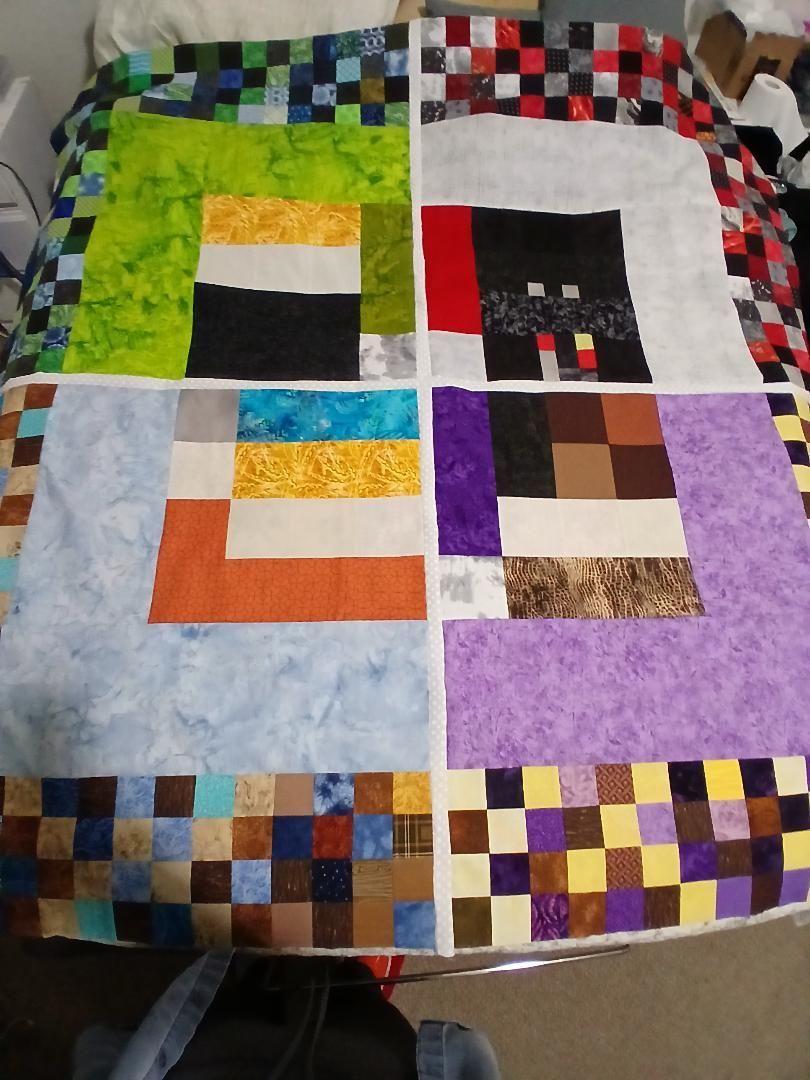 Colorful patchwork quilt with six square blocks in green, black, red, orange, purple, and brown on a table