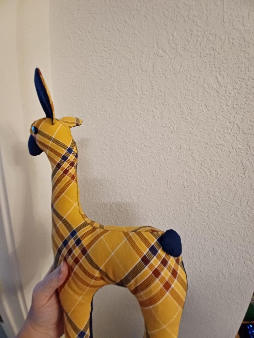 Handmade yellow plaid deer figurine with navy accents, held upright against a white wall