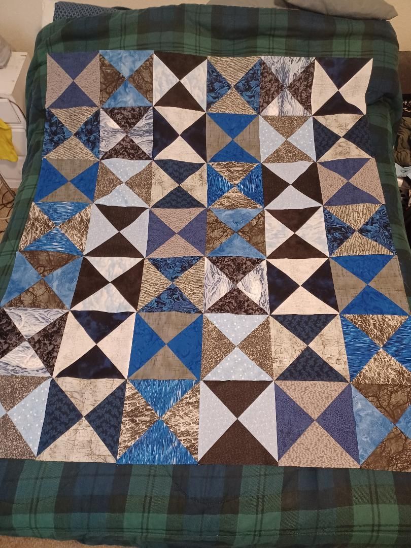 Blue, white, and brown patchwork quilt with triangle patterns on a green plaid background.