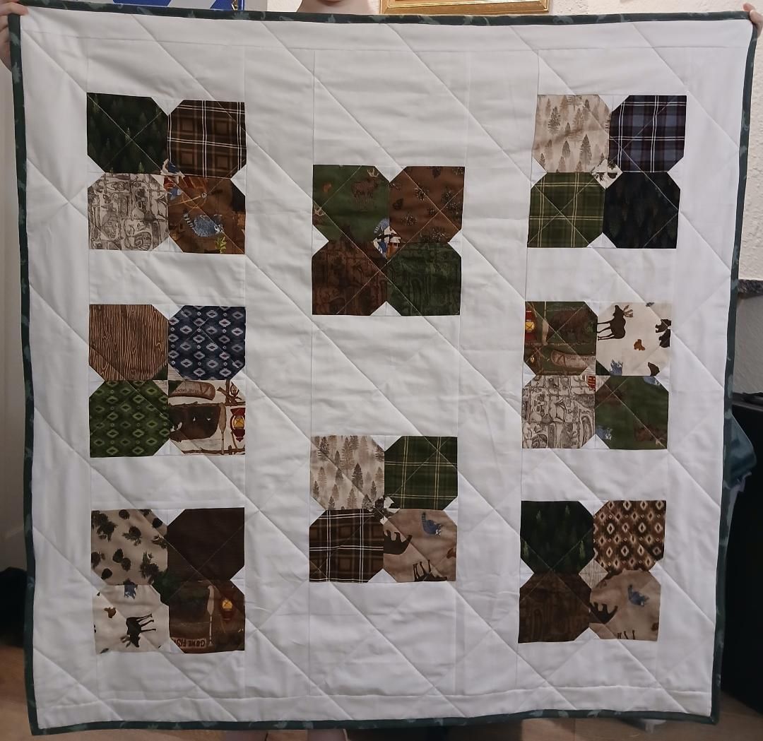White quilt with scattered patchwork squares in earthy green, brown, and plaid patterns.