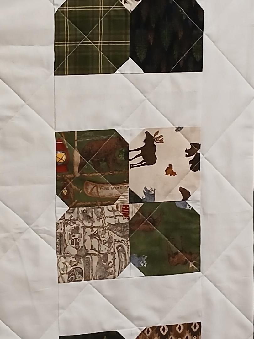 Close-up of a quilt with patchwork squares in green, brown, and tan patterns and a cat silhouette block