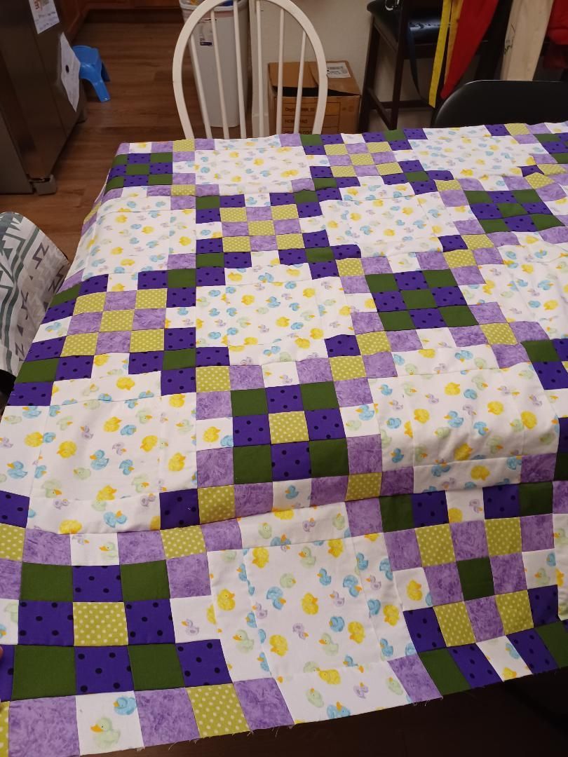 Purple, green, and white quilt with floral squares spread over a table in a dining room