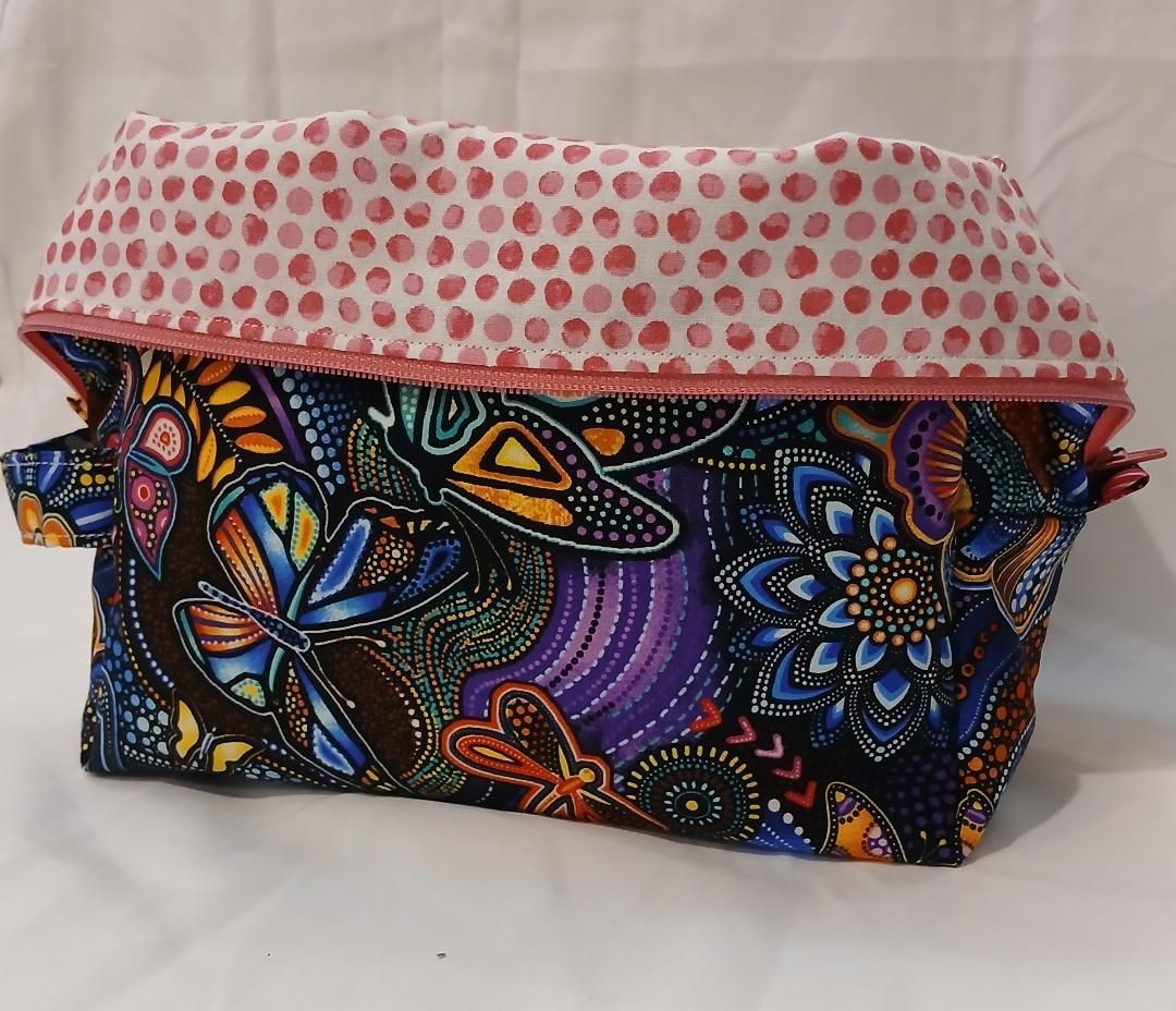 Colorful floral-patterned fabric zip pouch with a pink polka-dot flap on a white background