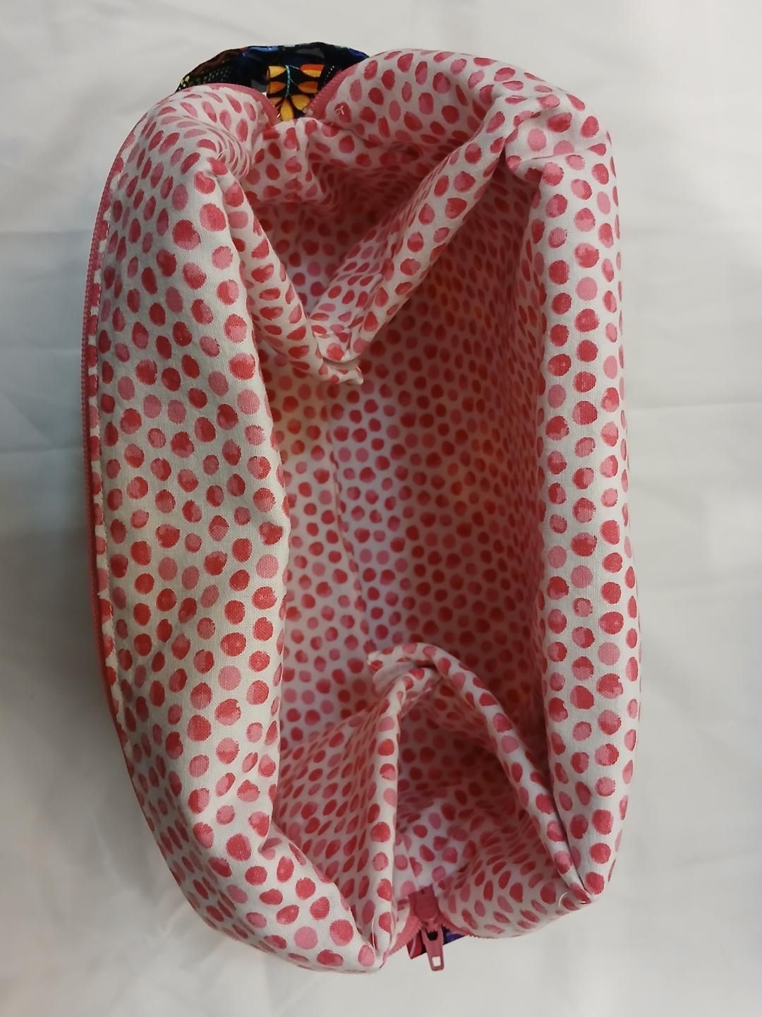Pink and white polka-dot fabric bag or backpack hanging open, front view