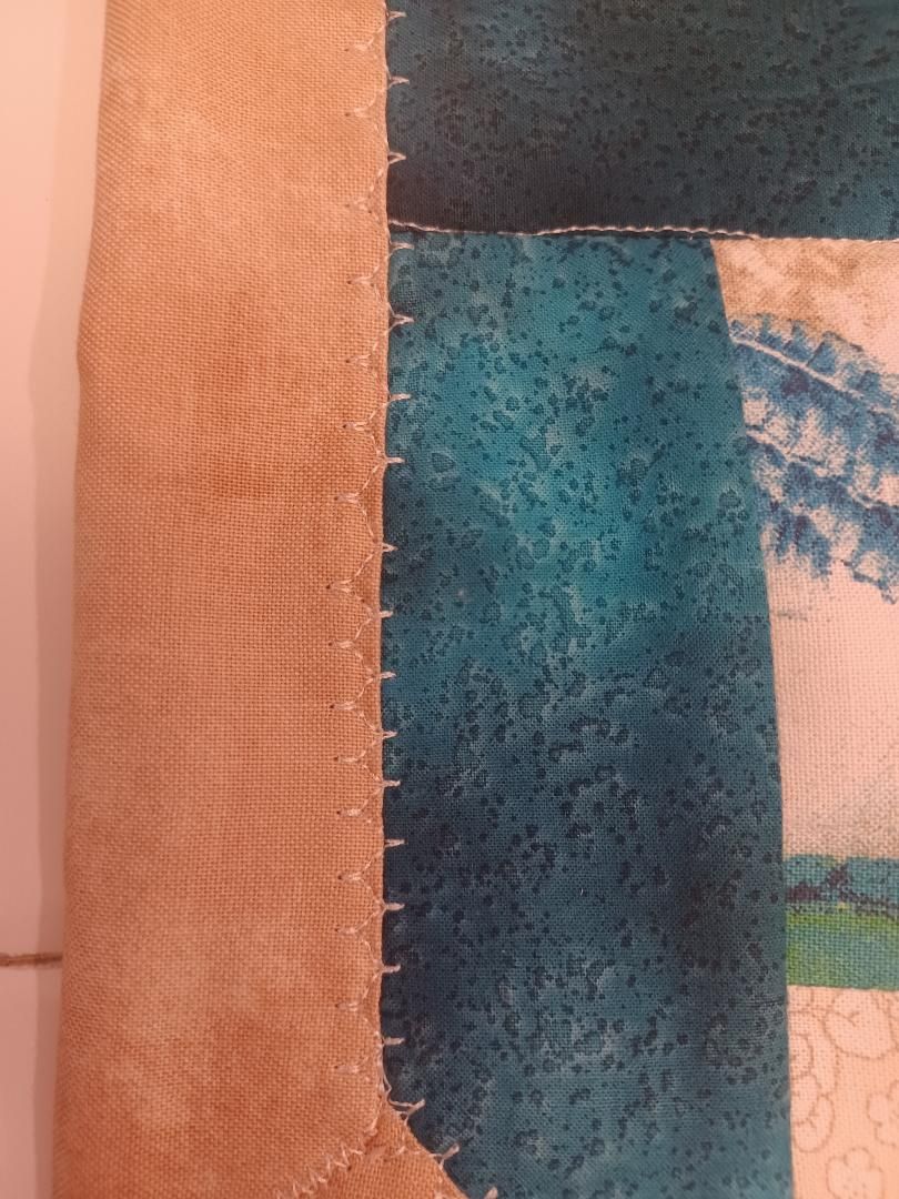 Close-up of a teal and tan textured fabric edge with a stitched seam and patterned background