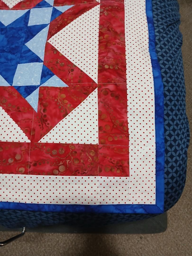 Close-up of a red, white, and blue quilt corner with star and dotted fabric patterns.
