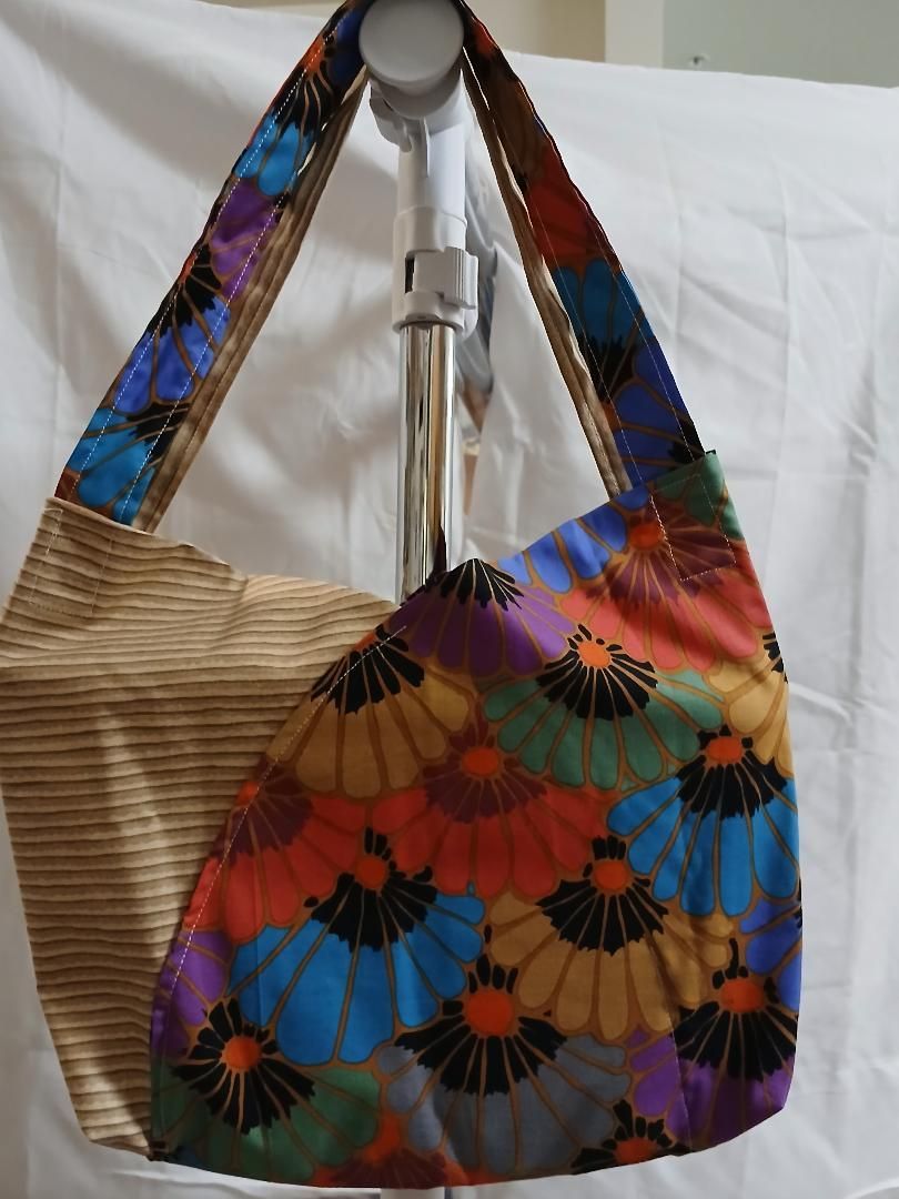 Colorful patterned tote bag with wide shoulder straps, hanging against a white background.