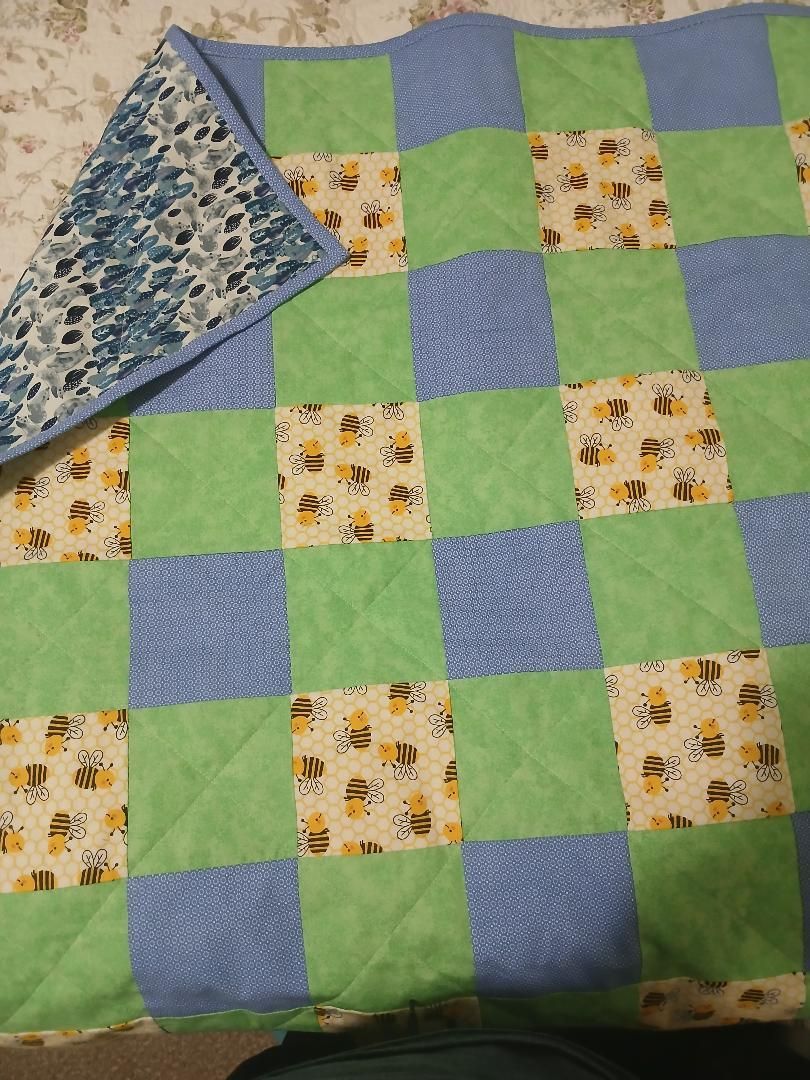 Blue-and-green checkered quilt with floral squares, folded corner showing blue patterned backing