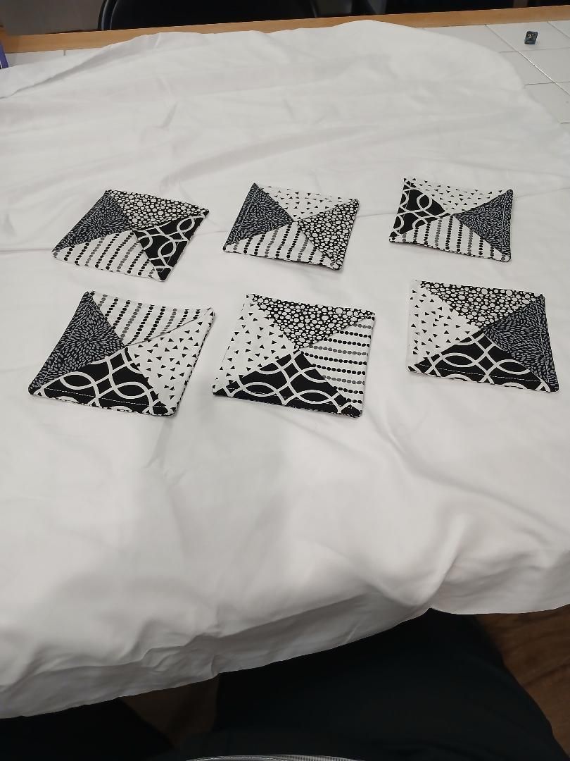 Six black-and-white patterned paper squares arranged on a white bedspread.