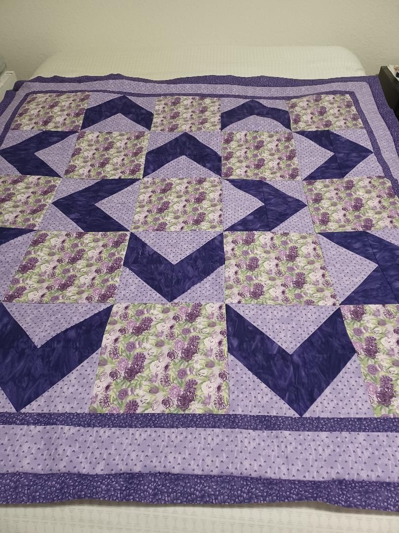Purple and lavender patchwork quilt with geometric star and chevron patterns on a bed