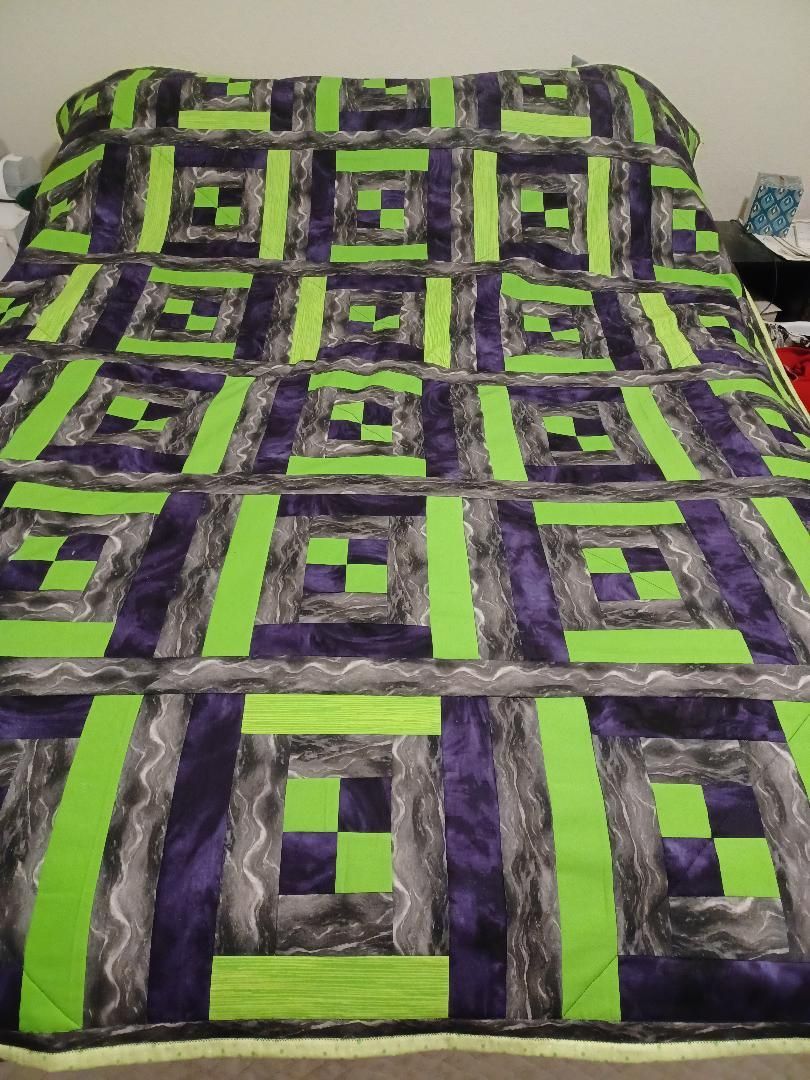 Purple and neon green geometric quilt with square block patterns laid on a bed
