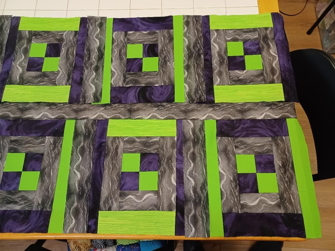 Patchwork quilt with purple, gray, and neon green geometric square patterns on a bed