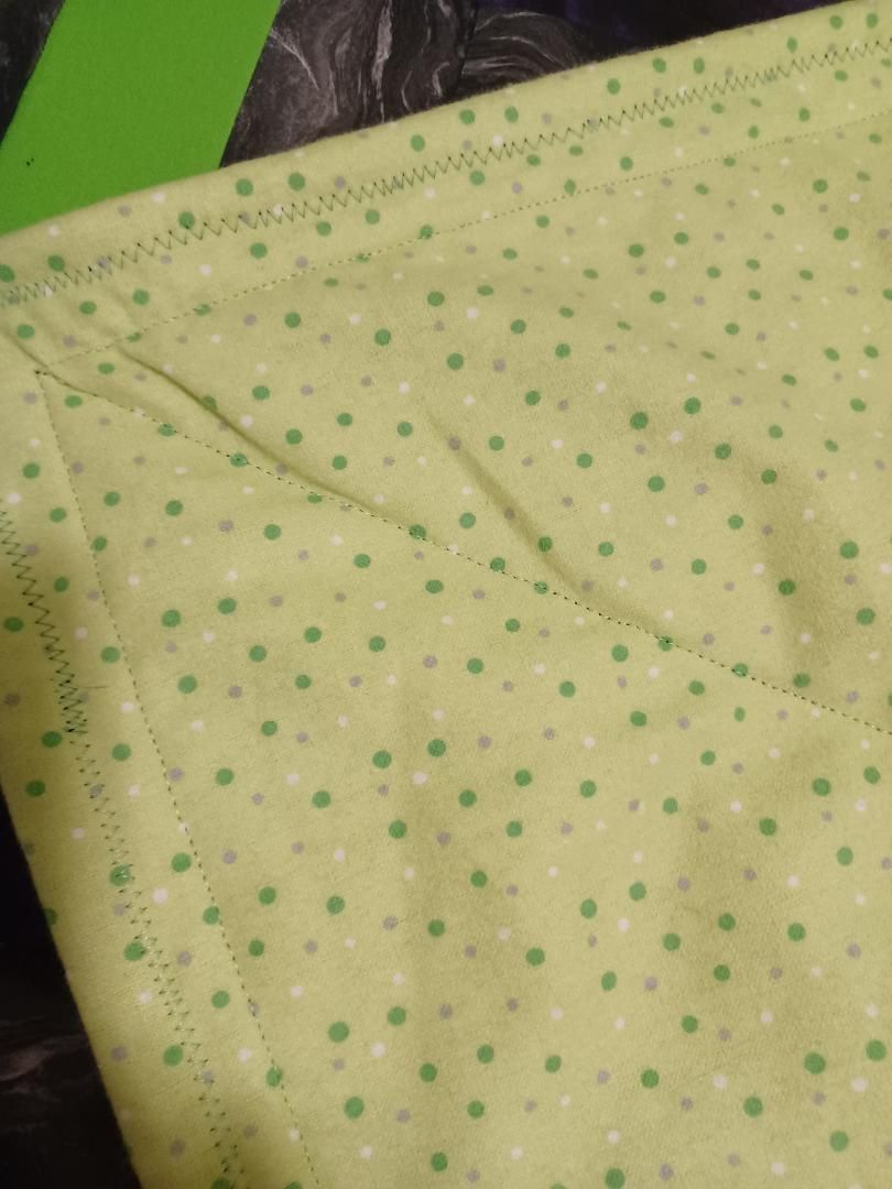 Light yellow fabric with small green polka dots and a diagonal seam detail