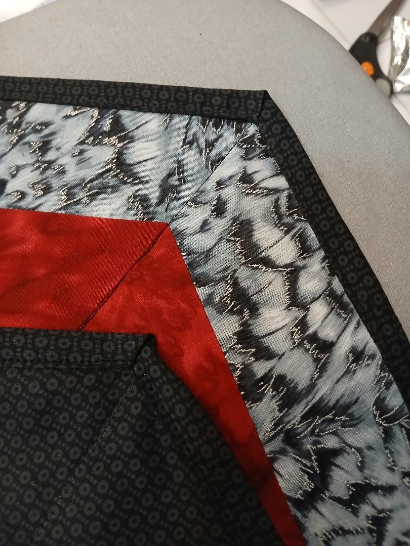 Close-up of a quilted fabric corner with red, black, and white patterned patches on a gray surface
