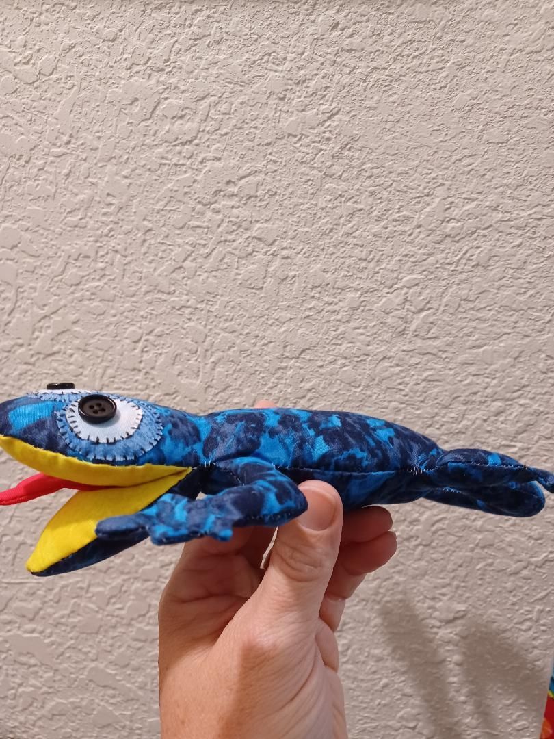 Hand holding a blue toy shark with yellow mouth and red fins against a beige wall