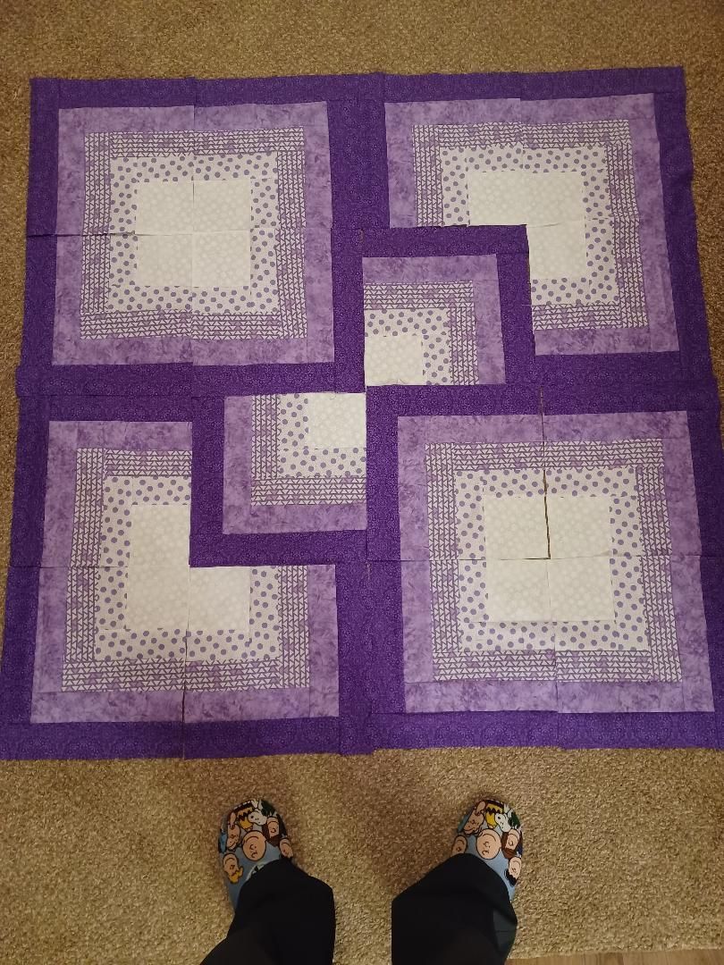 Purple and white geometric rug on beige carpet, with two shoes visible at the bottom.