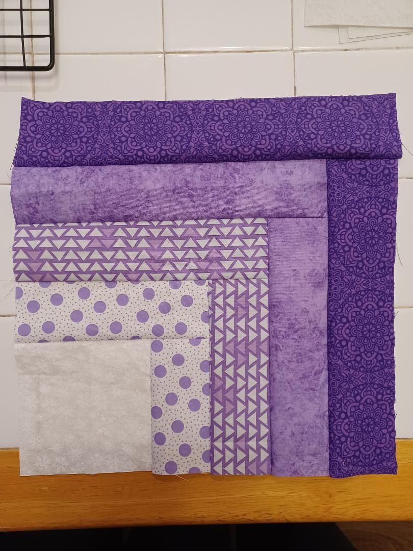 Stack of purple and lavender patterned fabric squares arranged in a layered quilt-like display.
