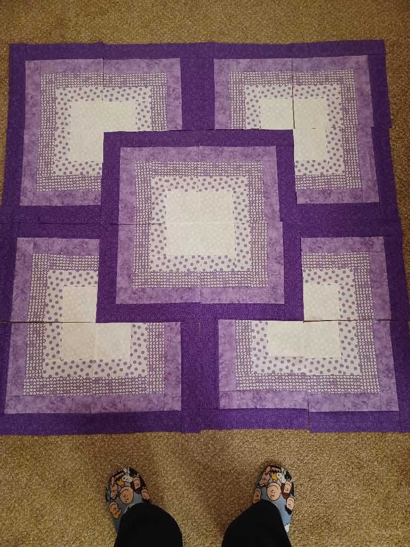 Purple and lavender geometric rug with layered square patterns on a tan carpeted floor