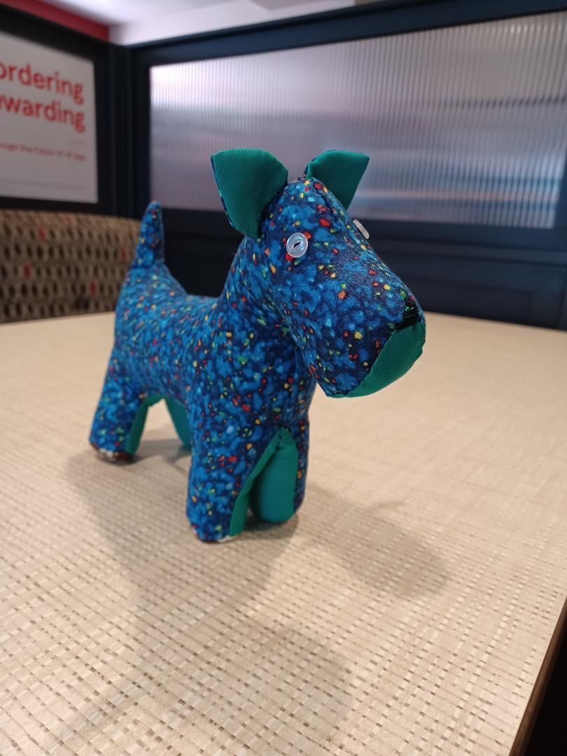Blue and green toy dog with a speckled pattern sitting on a table indoors