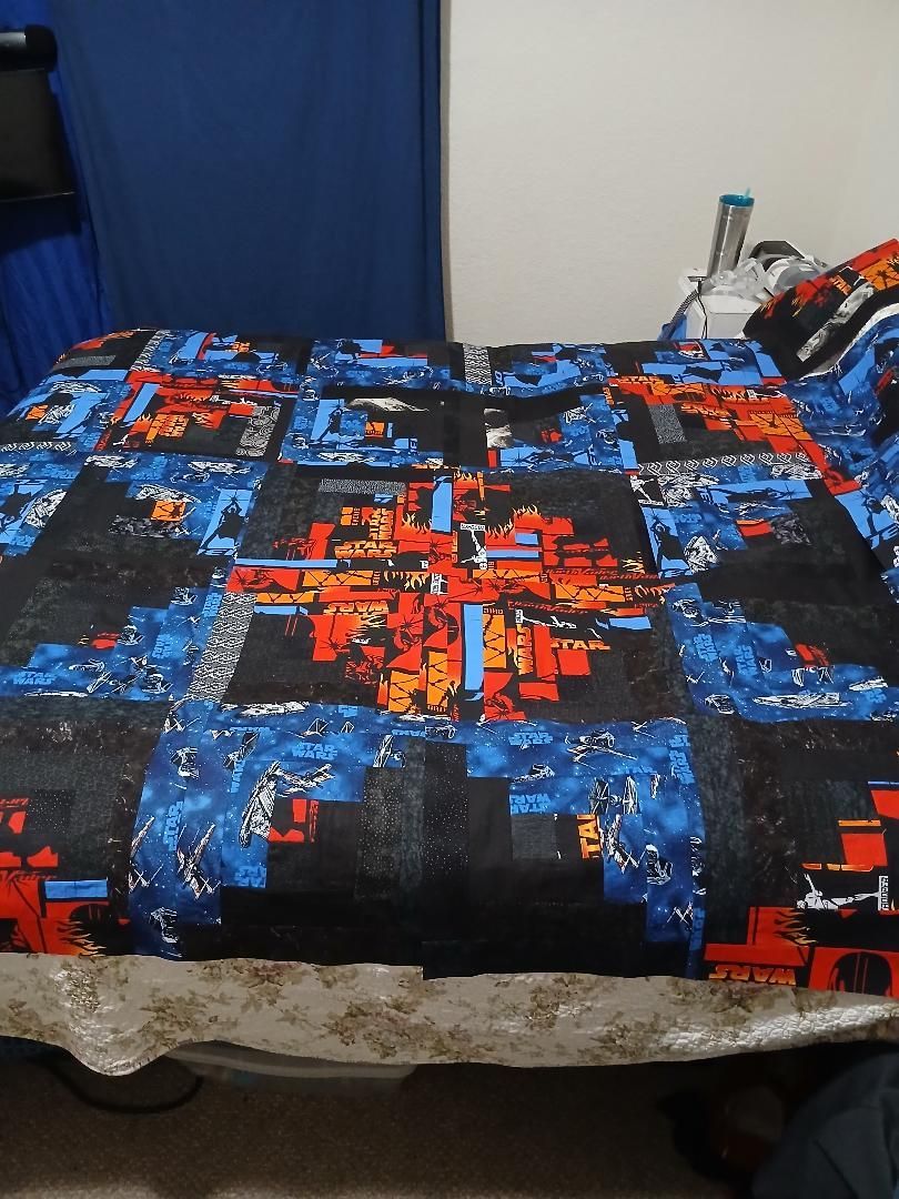 Bed with a blue, black, and red patterned blanket in a bedroom corner