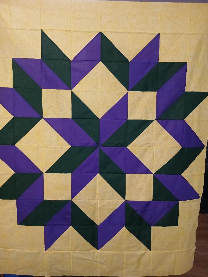 Geometric quilt pattern in purple, dark green, and beige on a cream background