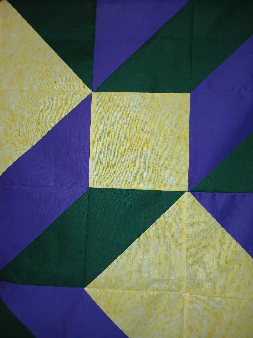 Abstract quilt pattern in purple, green, and pale yellow geometric triangles and squares.